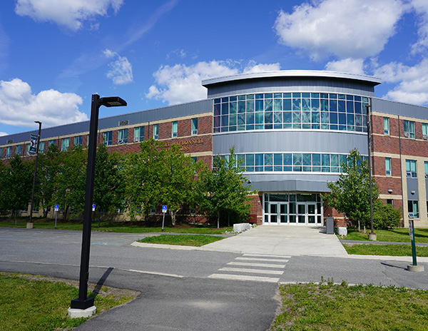 A brick building with a glass entrance is shown against a blue sky with puffy white clouds.