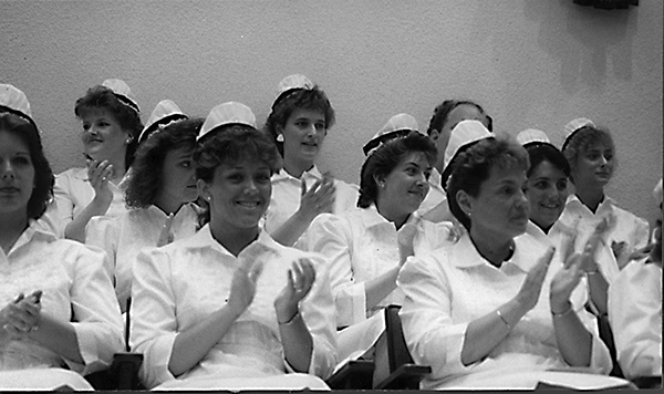 Women in white dresses and hat sit together in this undated photo. They are wearing vintage nursing uniforms common at the time.