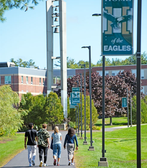 Students walking towards the bell tower on the campus of Husson University