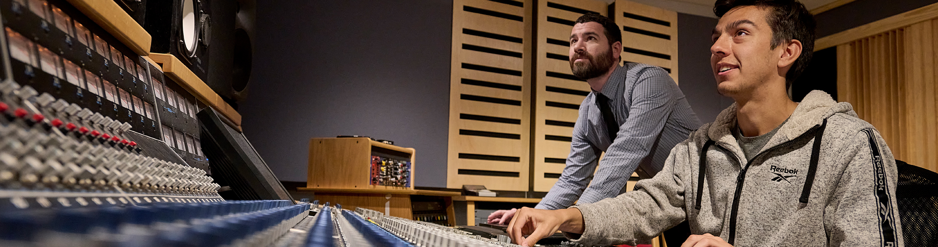 A student works in an audio engineering lab on an audio console with a faculty member