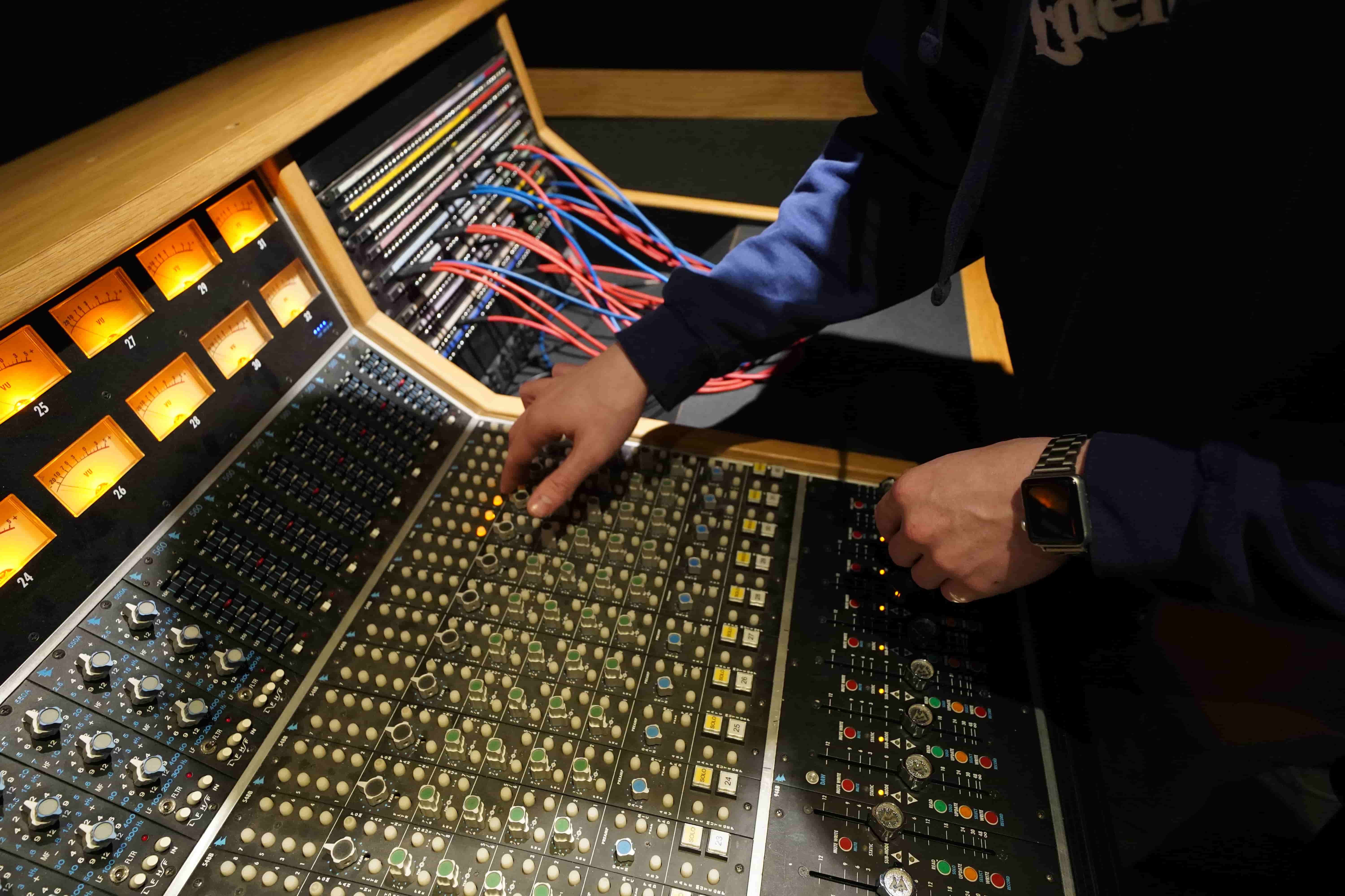 Close up image of an audio engineering students hands while they toggle knobs on an audio mixing console. 