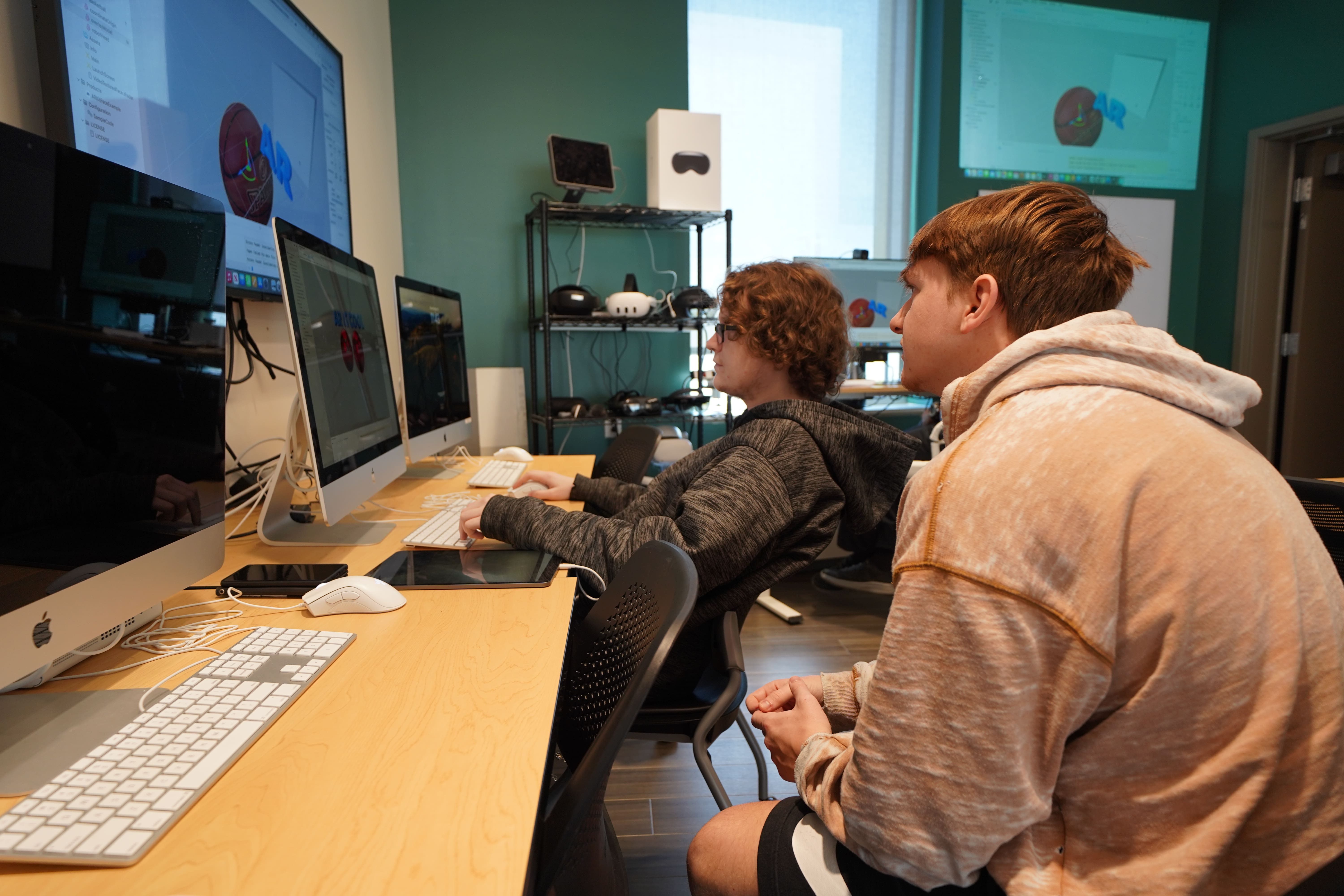 A student watches another student working on a computer in a university classroom.