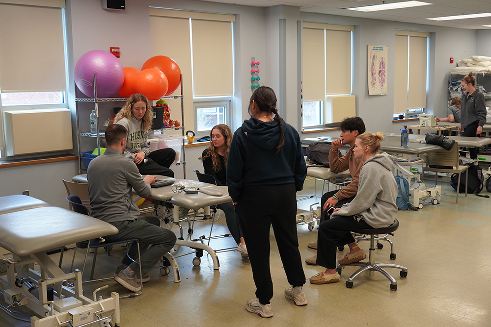 Professor instructing a group of students who are gathered around a physical therapy bed.