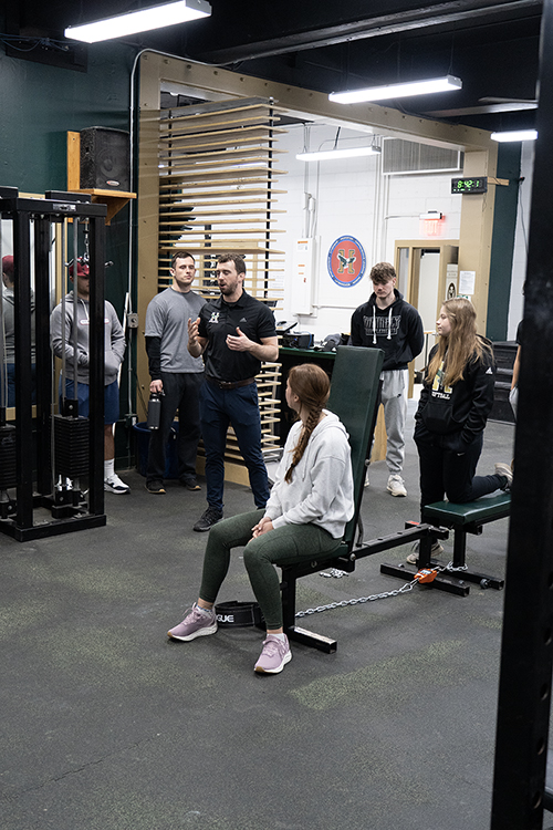 Students work in a weight room with faculty