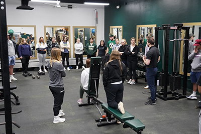 Students work in a weight room with faculty