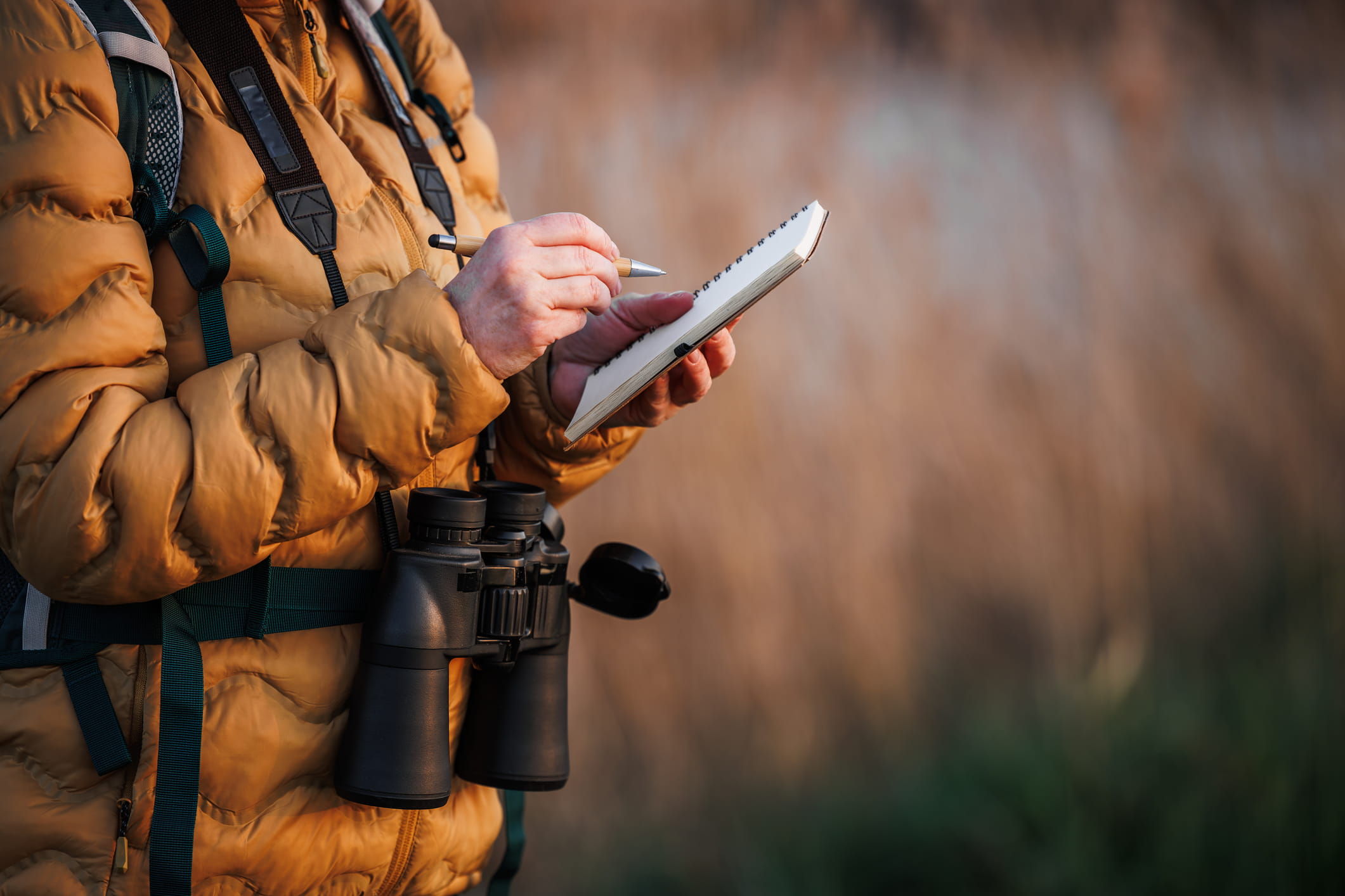 Person with binoculars writes in a field journal.