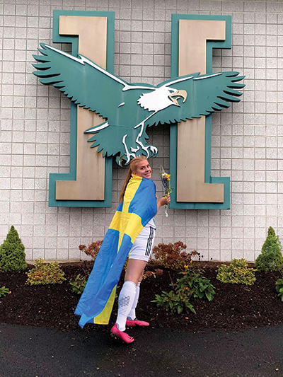 Maja Elsa Hoglund posing in a graduation gown in front of a Husson sign