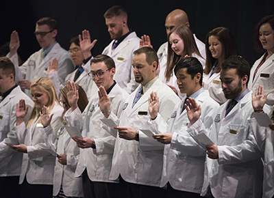 students wearing white coats read off pieces off paper