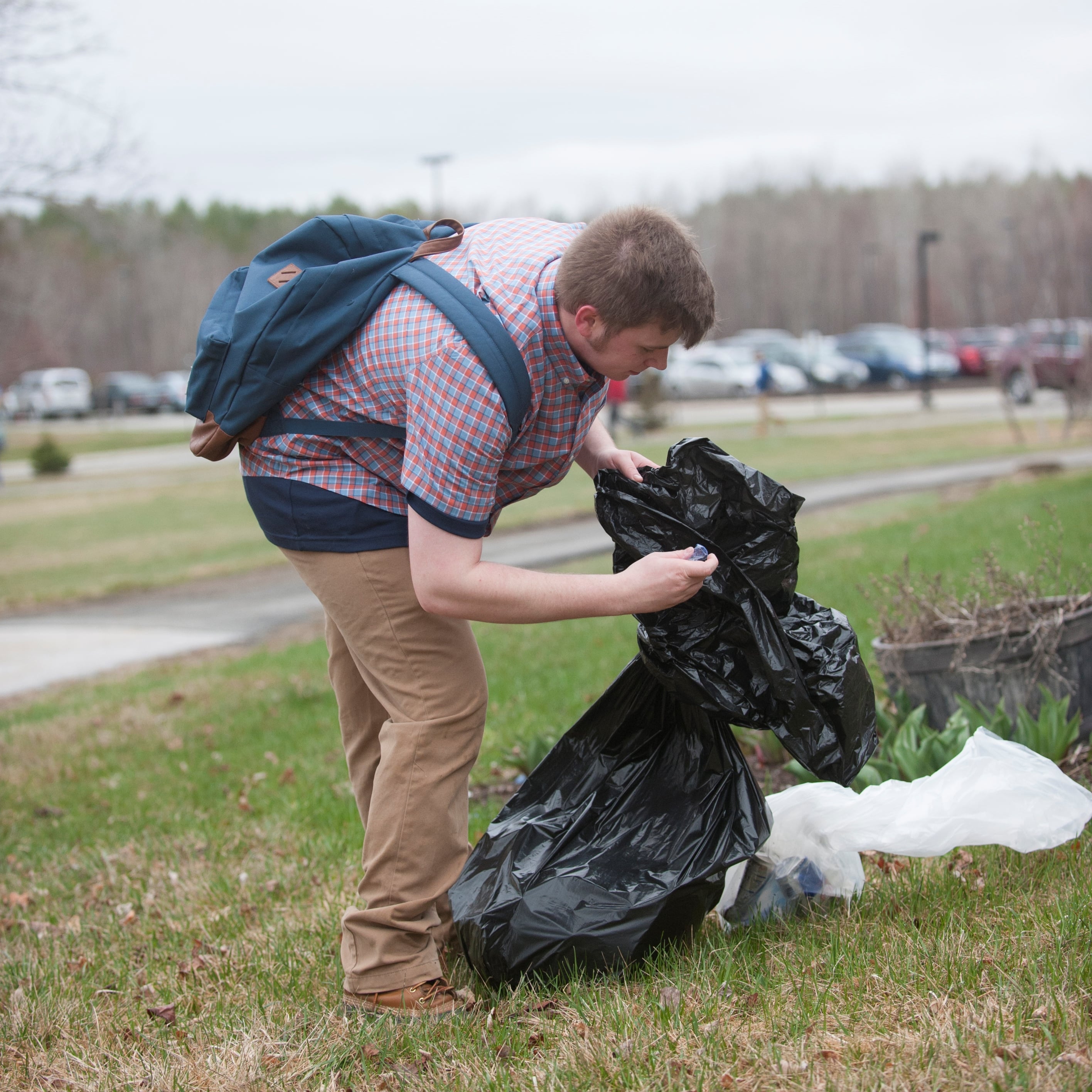 man holding a trash bag while picking up trash outside