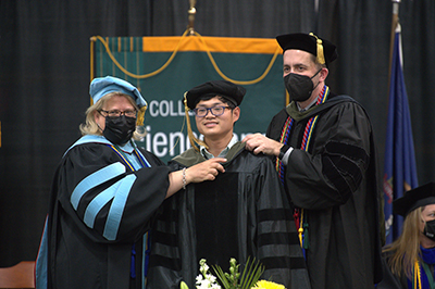student standing with Husson staff and faculty during hooding ceremony