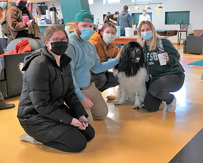 four people kneeling beside a dog