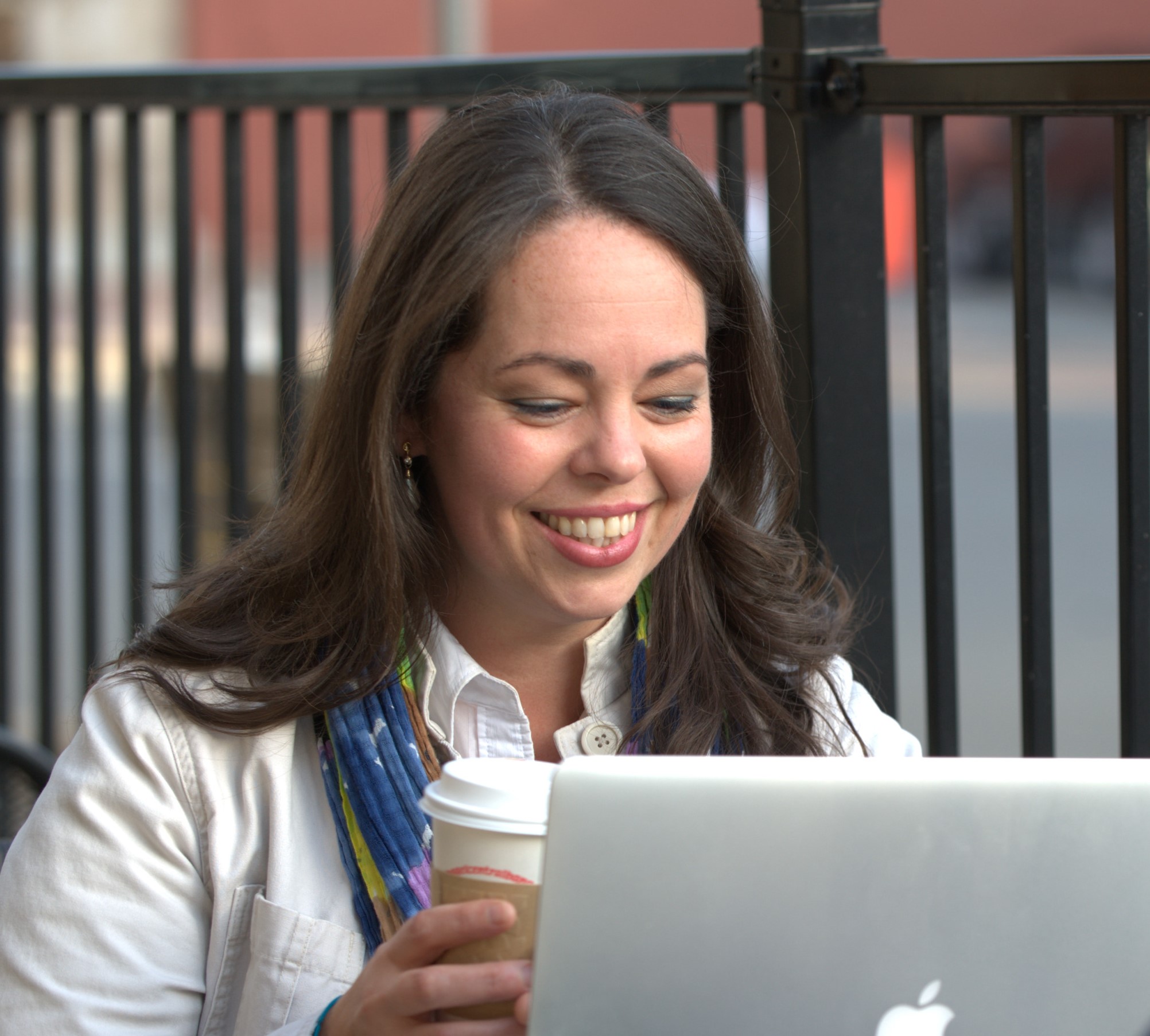 woman smiling while working on a laptop and holding a cup of coffee