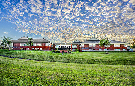 Image of MMG Insurance headquarters. The image features the brick MMG building, a green lawn, and a bright blue sky with small white clouds. 