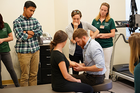 A Physical Therapist looks at a patient's arm and others observe.