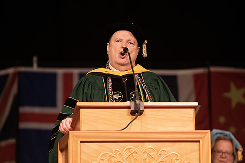 President Robert Clark of Husson University is shown in a cap and gown speaking at a podium at Commencement 2023.