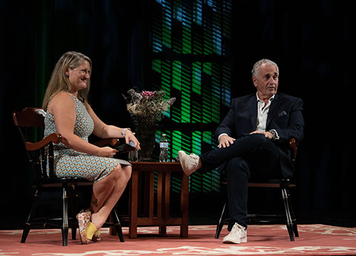 Dean Marie Hansen is shown seated on stage at The Gracie Theatre in Bangor, Maine, alongside Maine businessman Sean Riley.