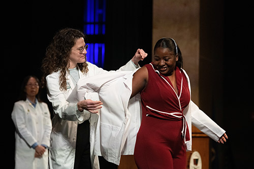A Husson University pharmacy student is helped into her white coat by a professor on the state at The Gracie Theatre in Bangor.