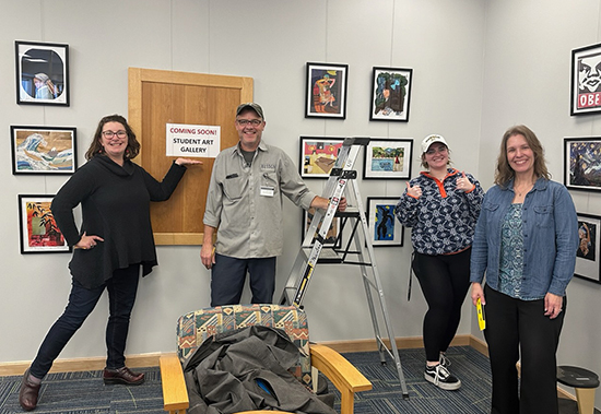 Three women and a man are shown in front of artwork hung on walls in the new Student Showcase Gallery at Husson University.