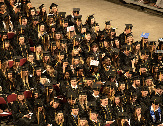 This photo features people in black caps and gowns seated in an auditorium.