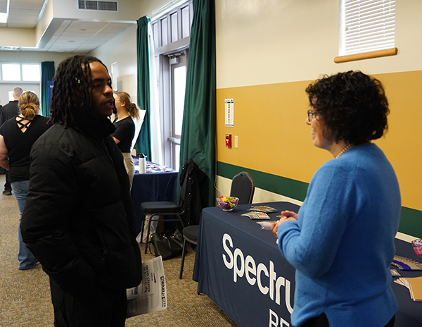 A man and a woman speak next to a table with the word "Spectrum" on it.