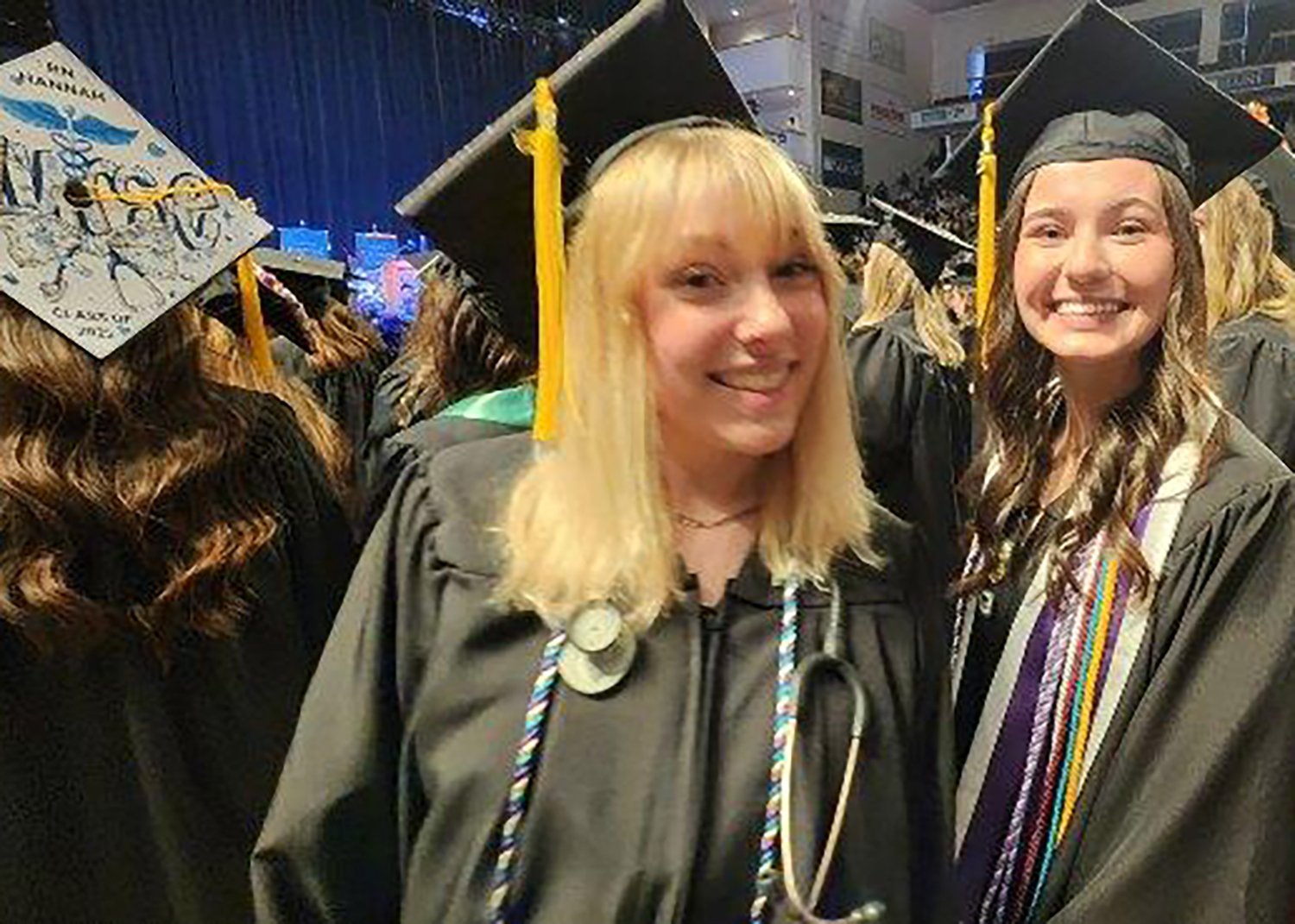 Smiling young people in caps and gowns look at the camera.