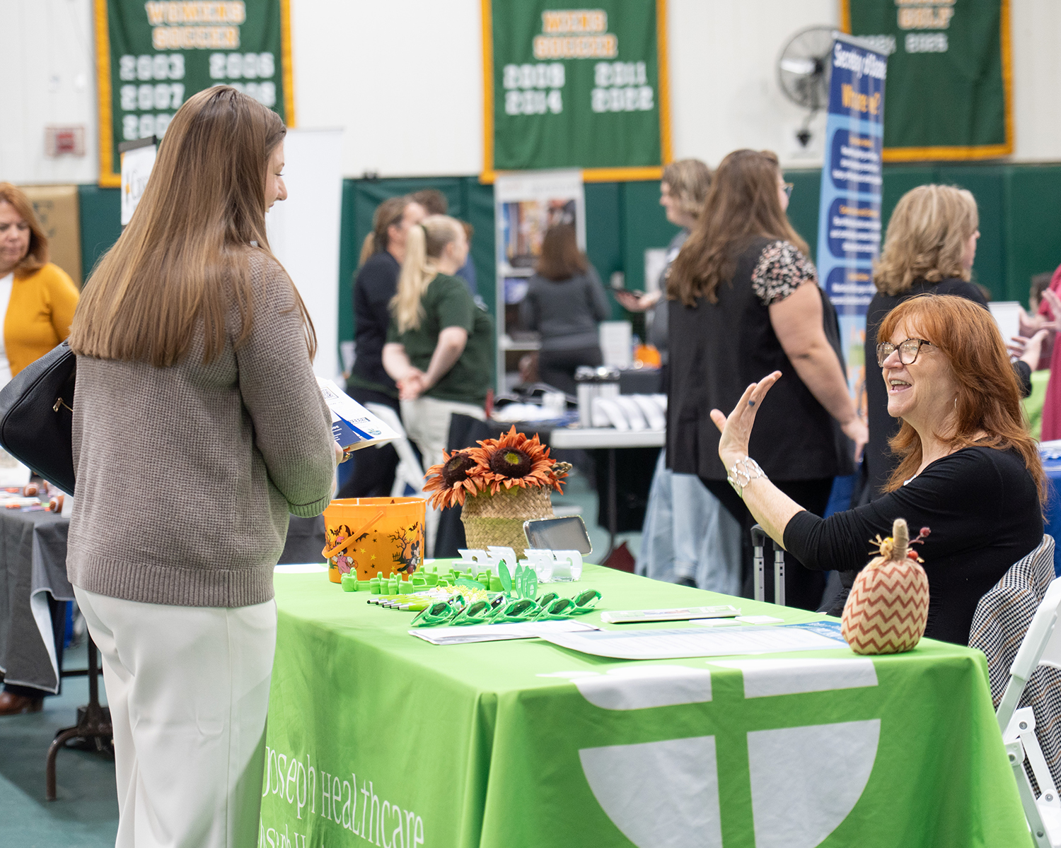 A group of people speak at a career fair. There are signs and tables around them.