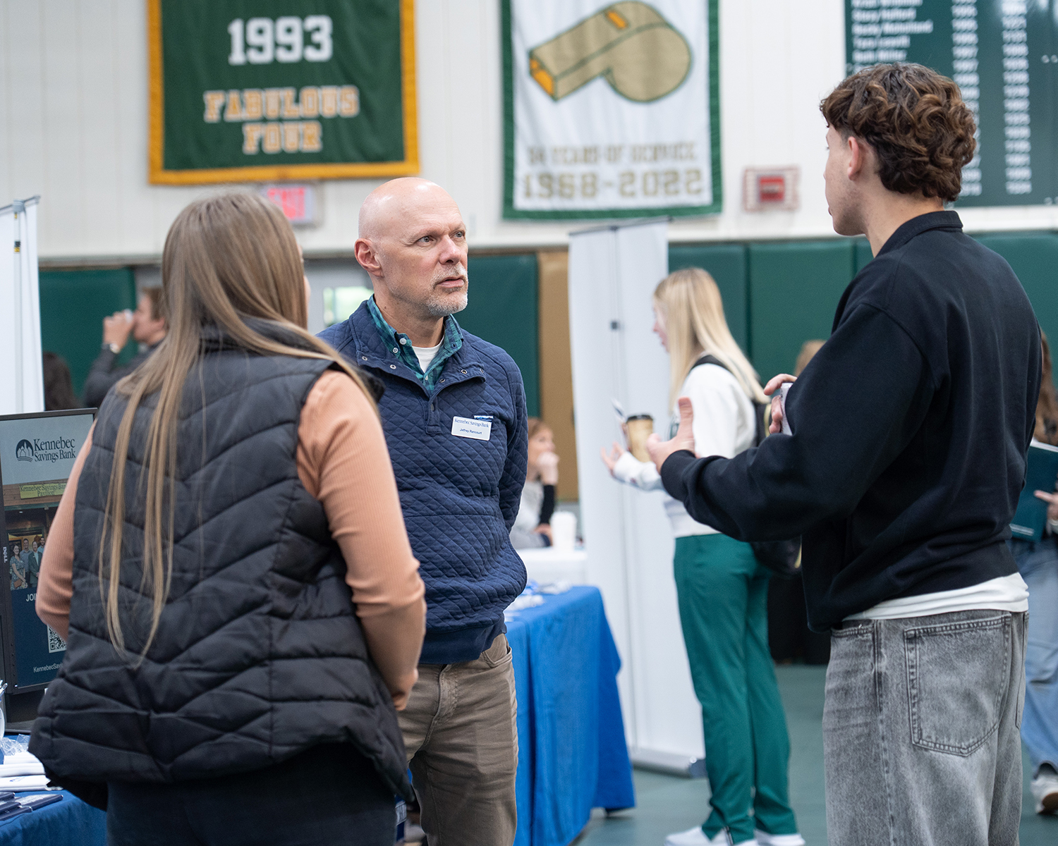 People talk at a career fair. There are tables and signs.