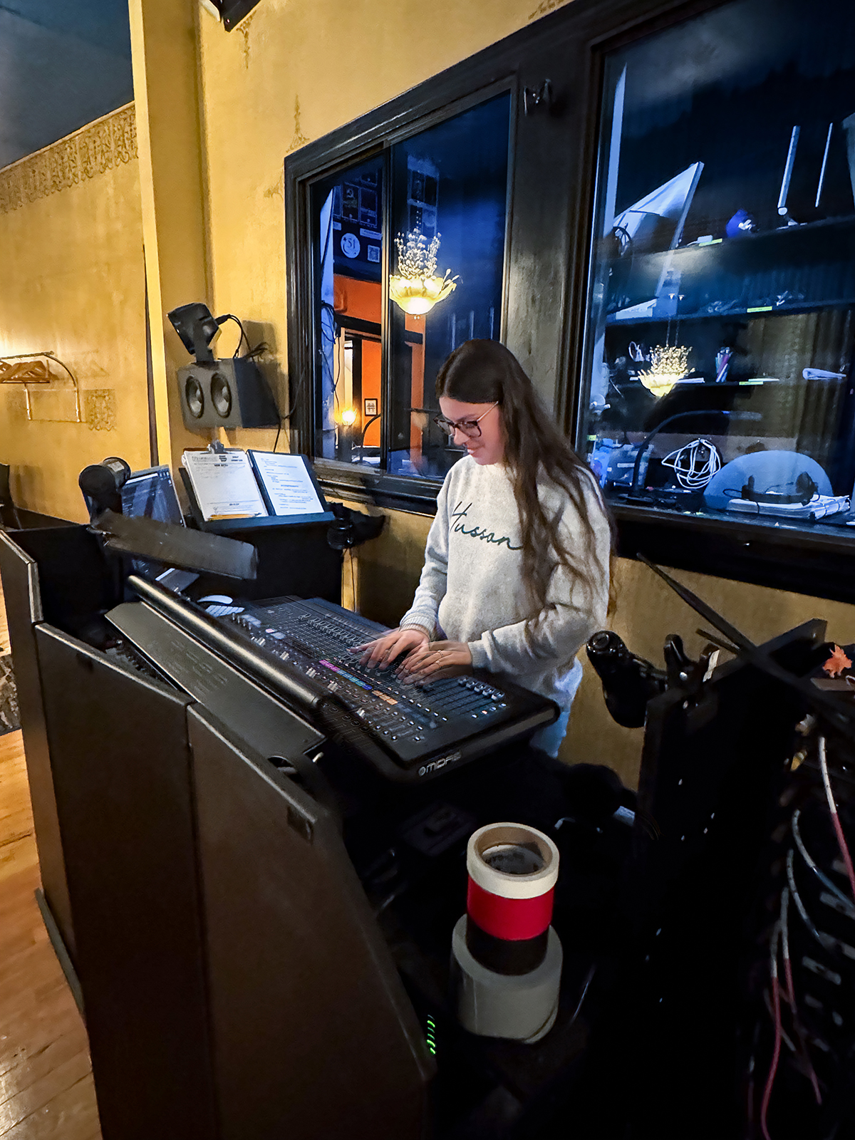 A young woman wearing glasses works at a sound board.