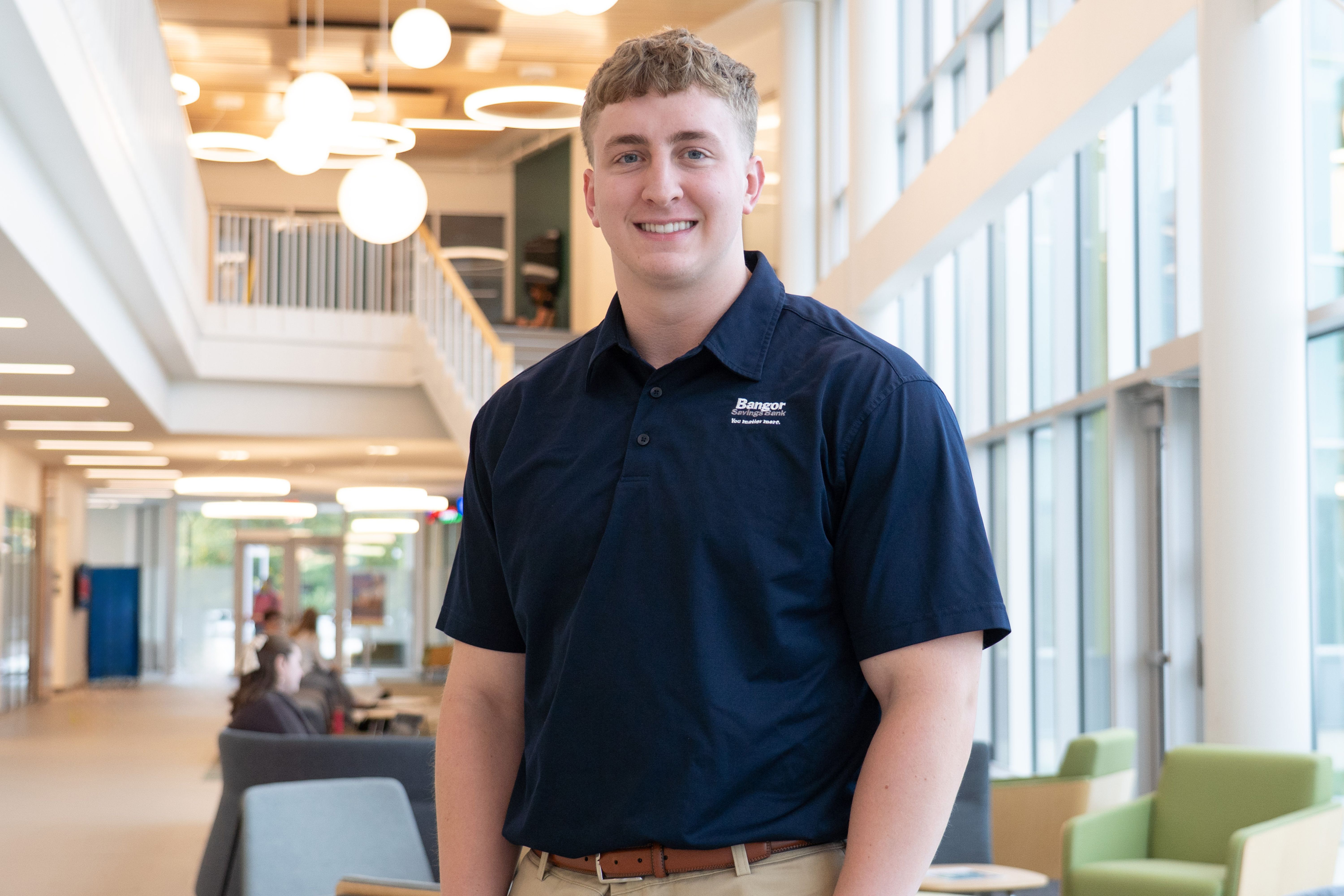 A young man in a polo shirt stands in a well-lit lobby.