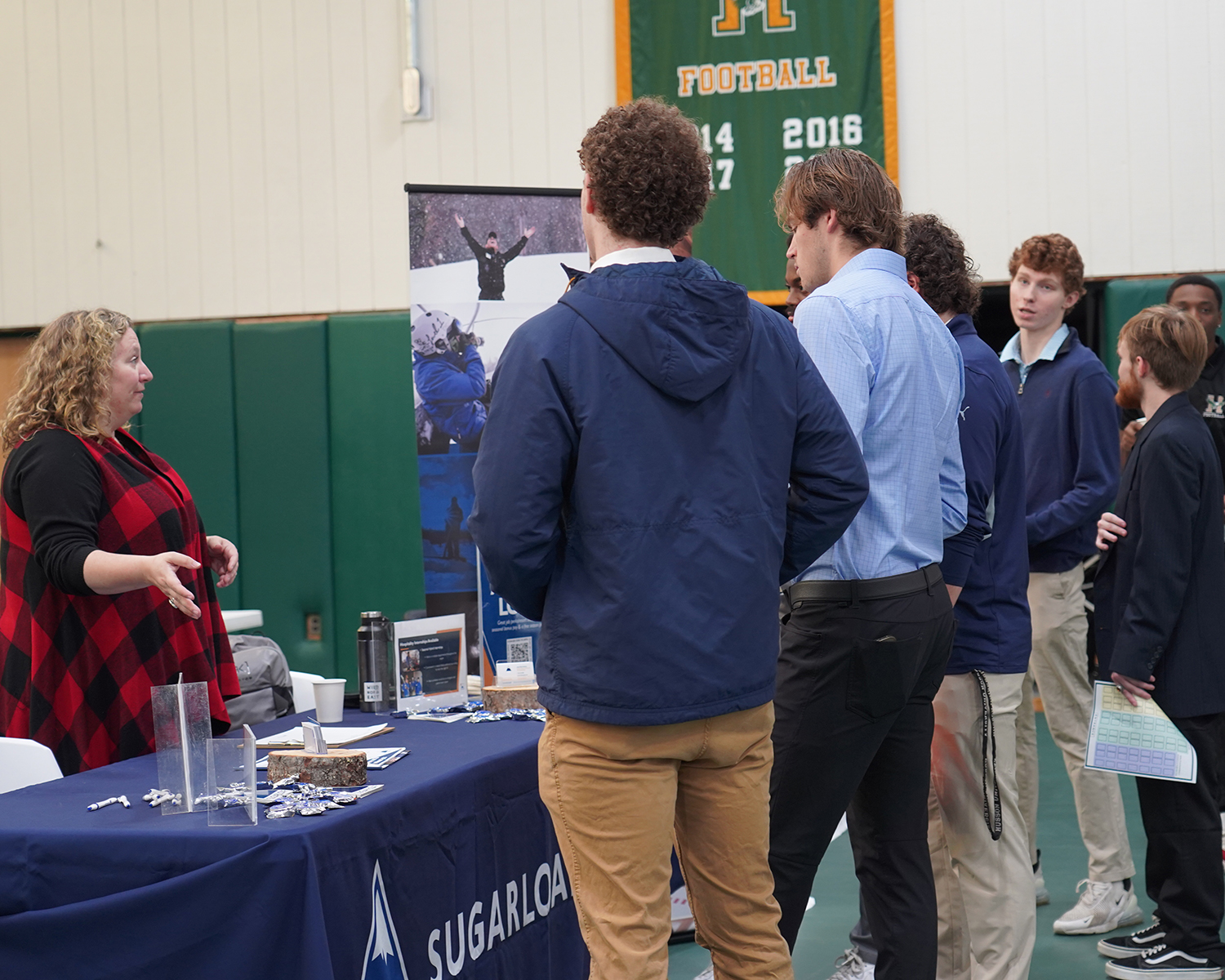 A group of young men talk to a woman behind a table at a career fair.