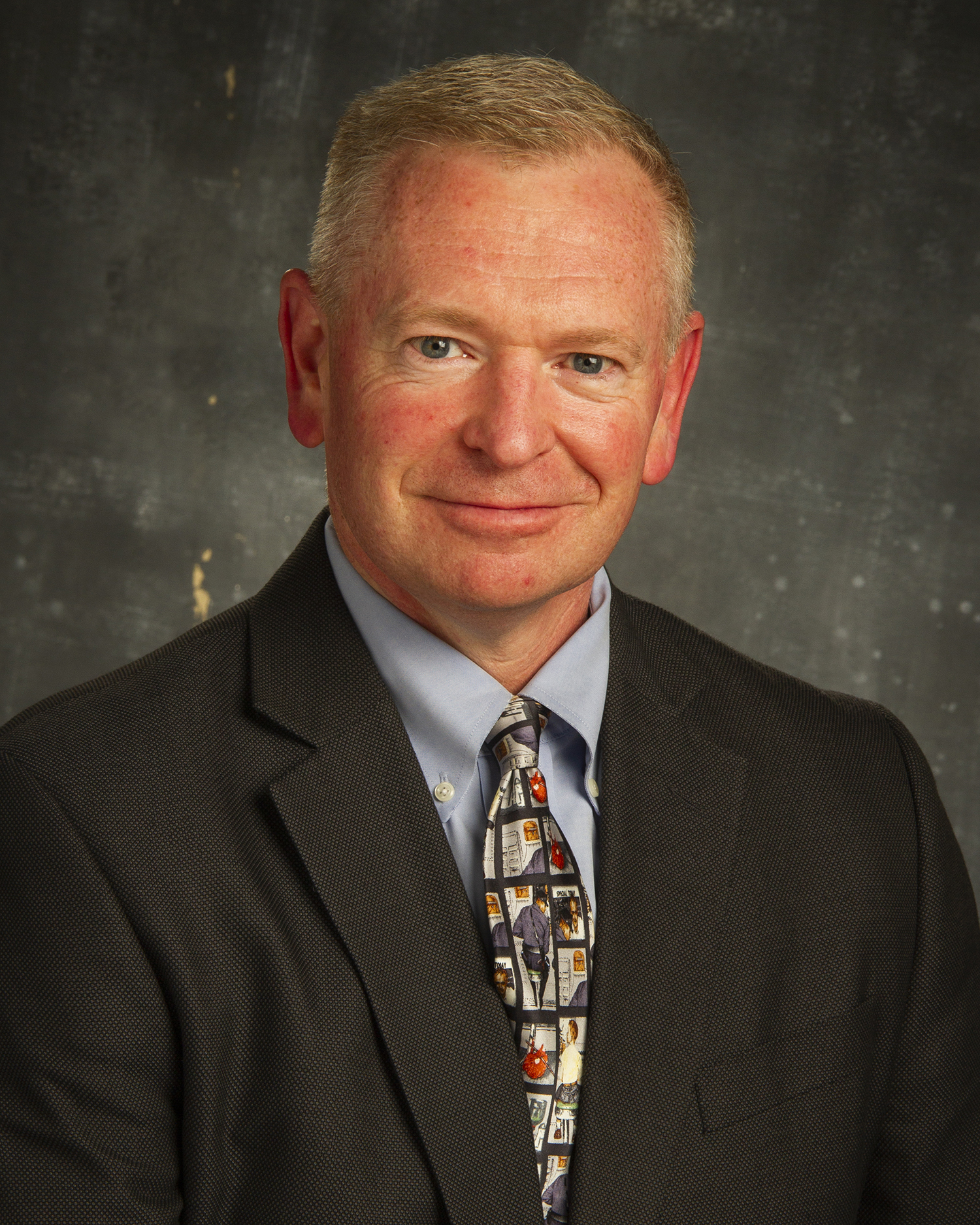 A headshot of a man in a suit is shown.