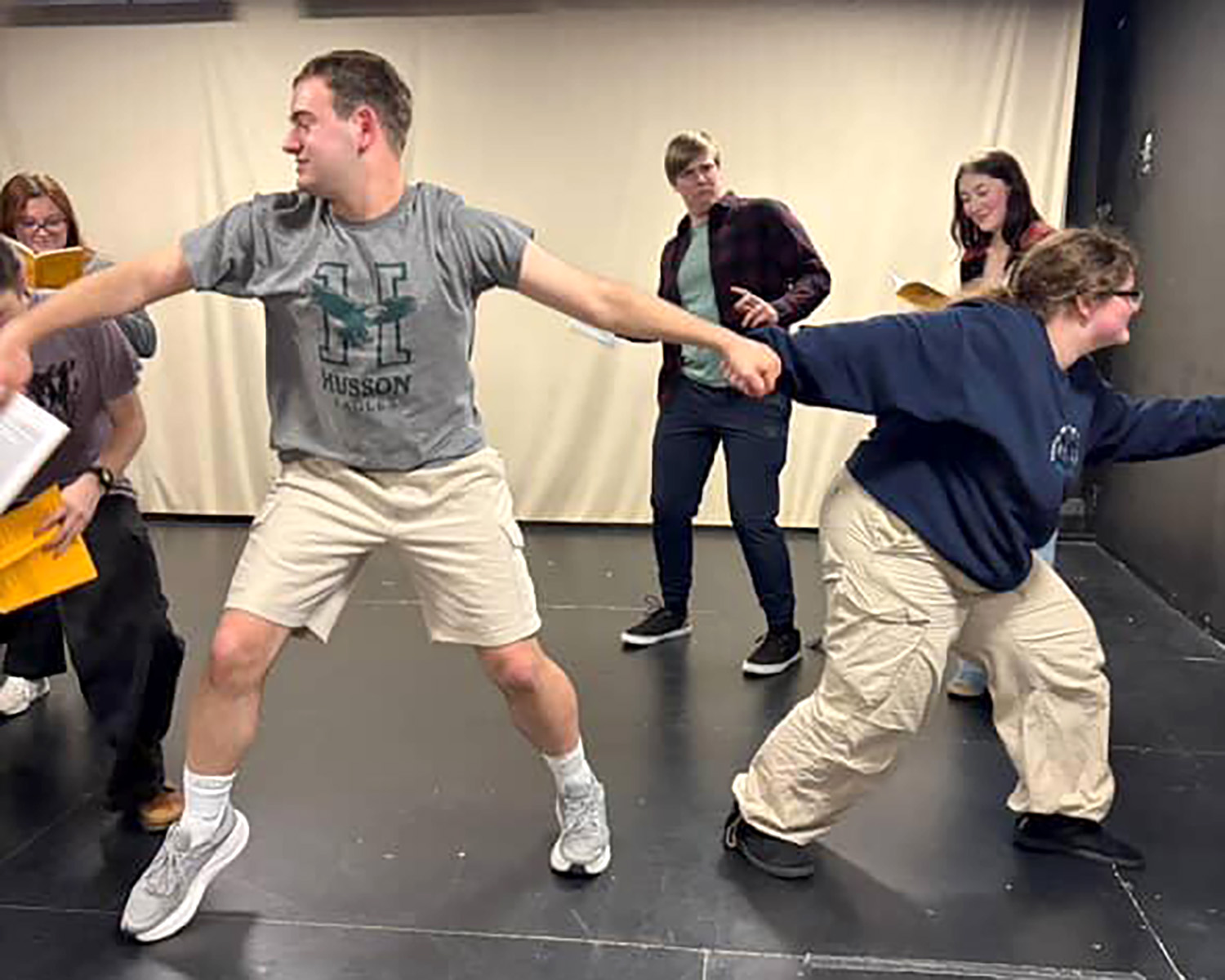 Students in an open space rehearse a scene by holding hands in a circle.