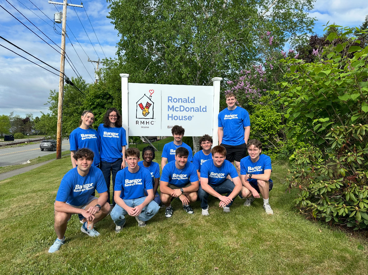 A group of young people wearing blue shirts are arranged around a Ronald McDonald House sign.