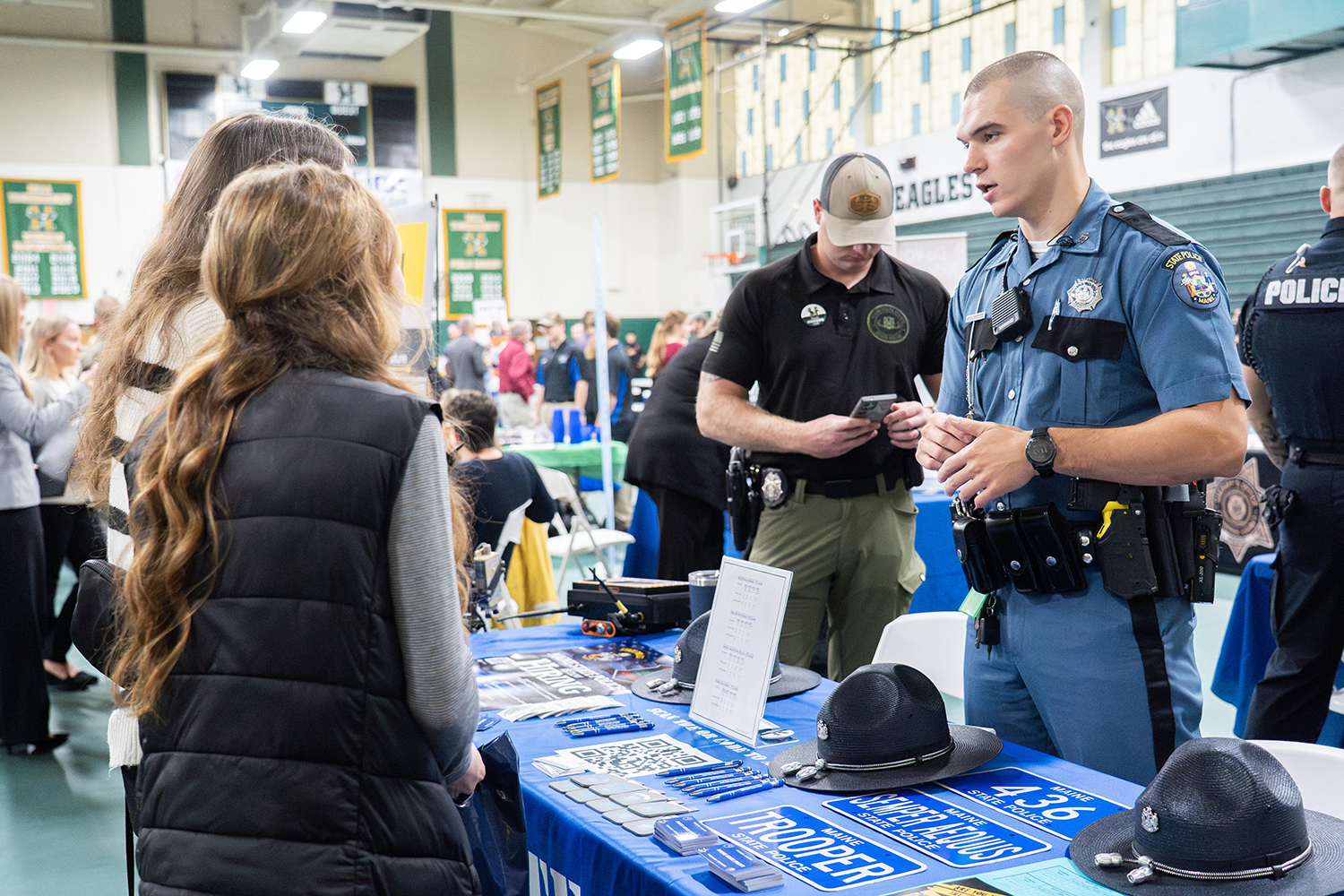 Two young women speak to men in uniform at a career fair.