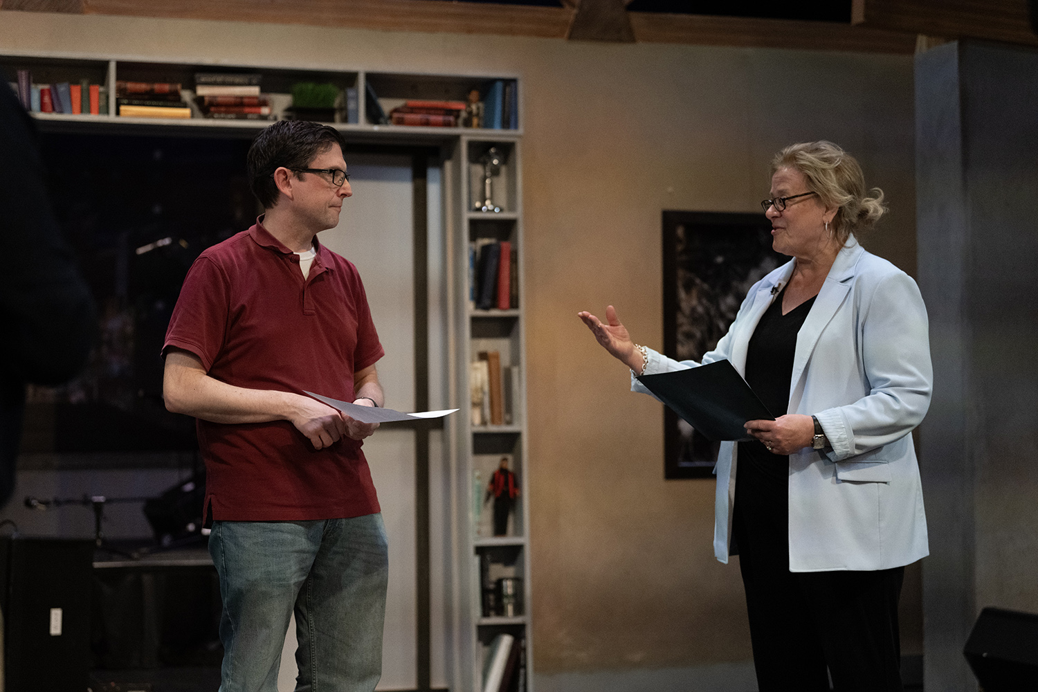 A man in a rust colored polo shirt and a woman in a light blue blazer interact on a television set.