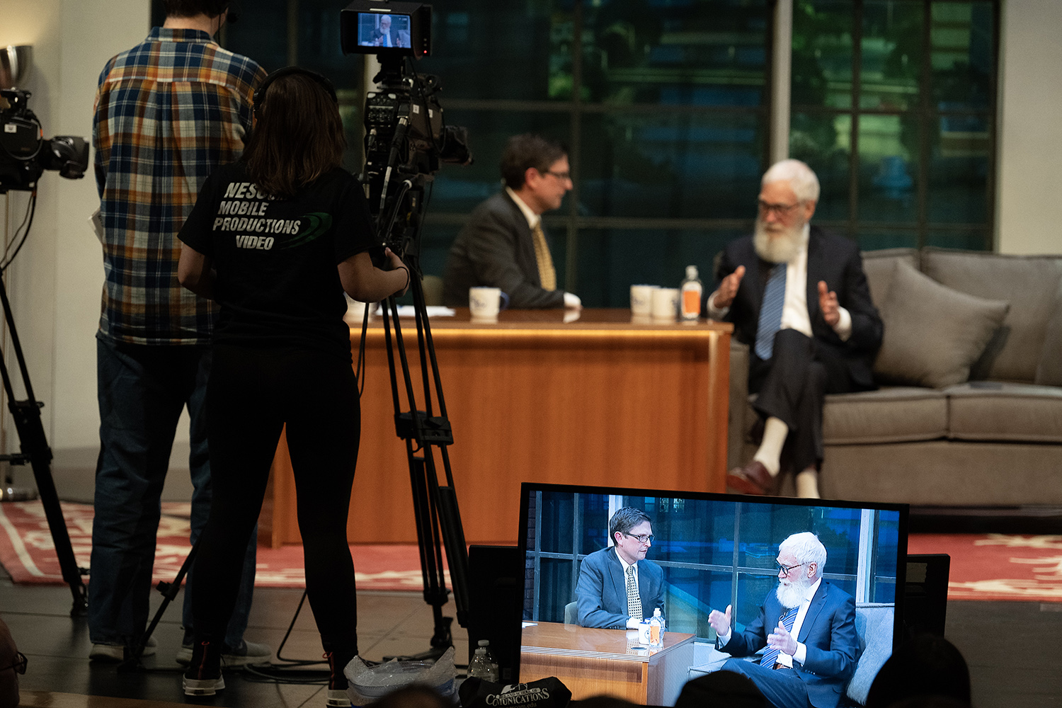 Two men on a television stage converse with smiles while the TV crew films.