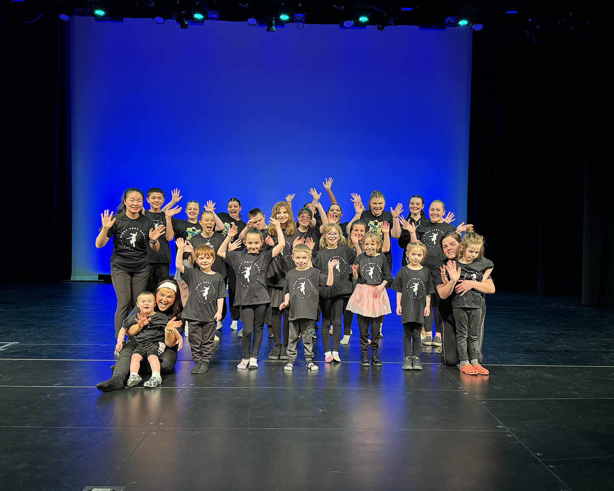 A group of children and adults stand together on a stage.
