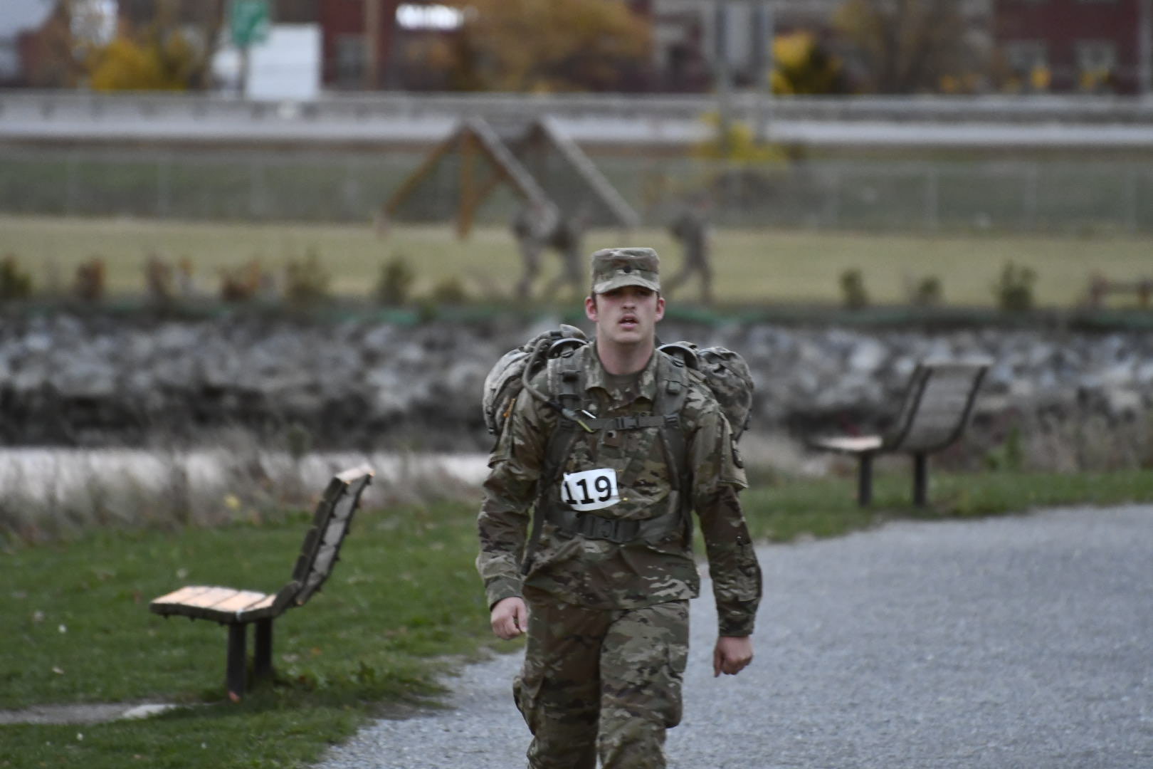 A man in fatigues writes on a road toward the camera.