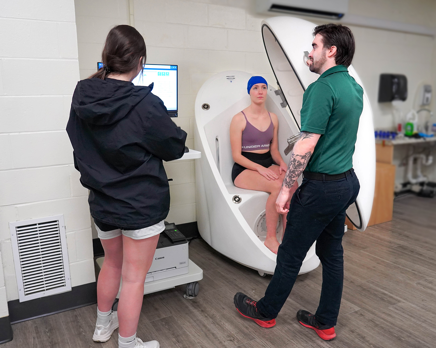 A young woman in a swim cap sits in a pod with other people instructing her.