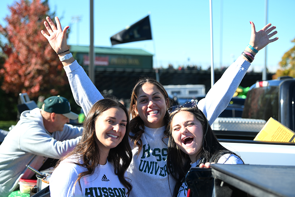 Two young women smile at the camera wearing Husson University logo shirts.