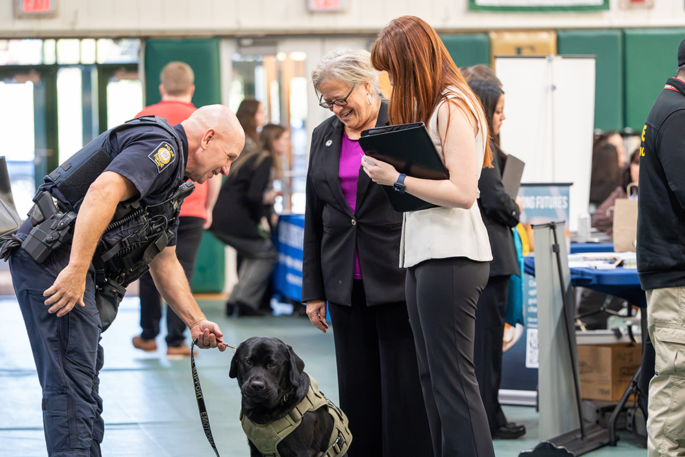 A member of law enforcement pets a black dog while others look on.