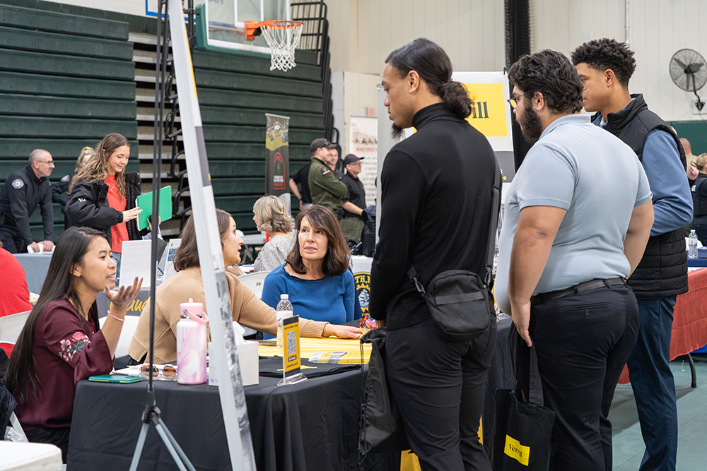 A group of people speak over a table at a career fair.