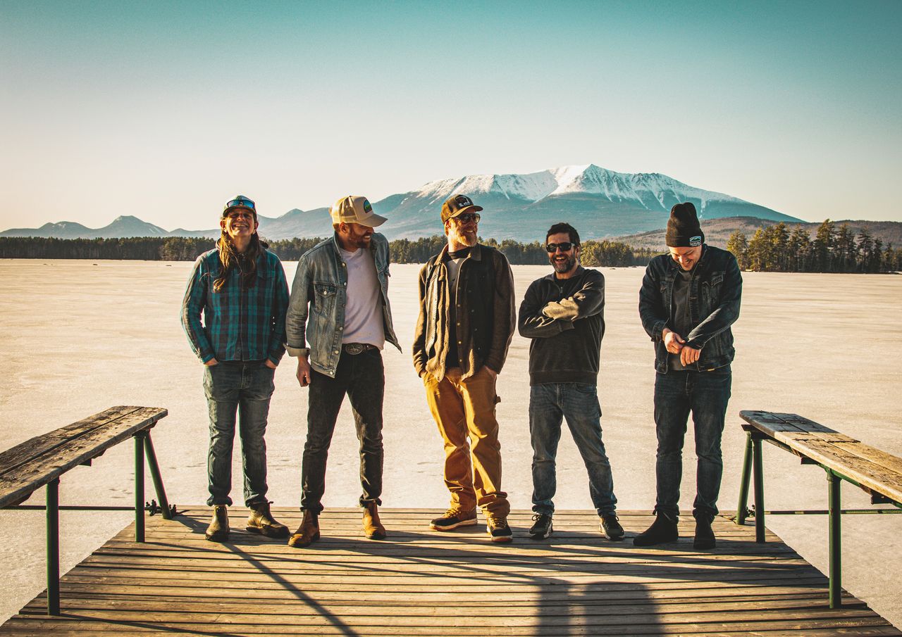 A group of men stand on a dock with the water in the background.