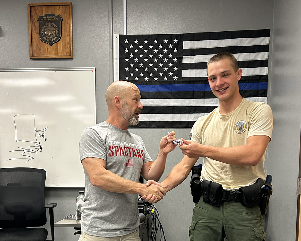 A smiling young man receives an award from a smiling man.