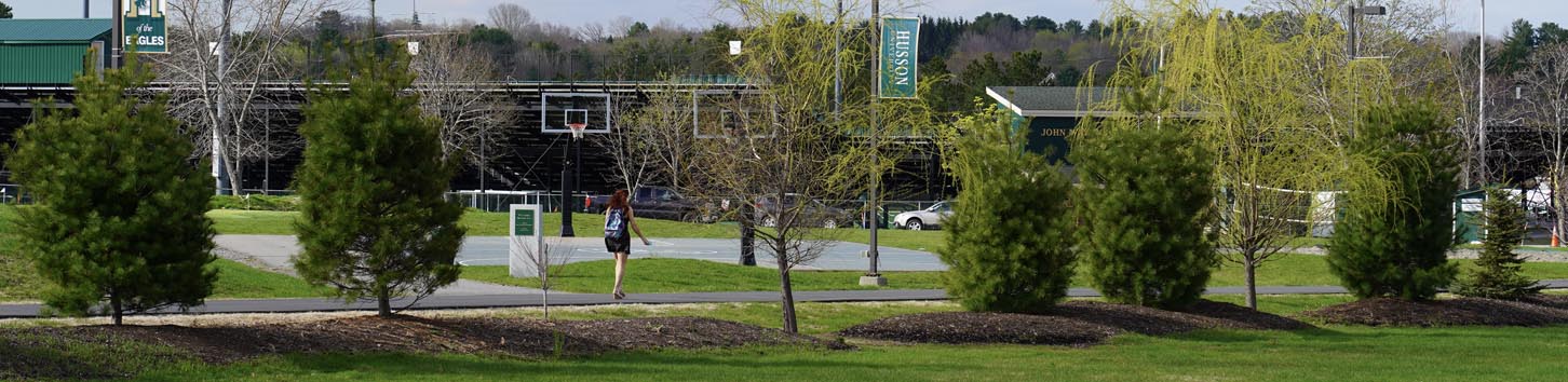 Basketball hoops and other sporting facilities on Husson University's campus are shown. There are trees and shrubs in the foreground.