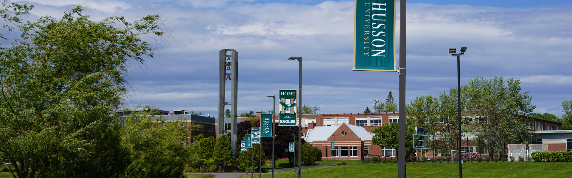 A winter scene on the campus of Husson University, with snow covered trees and the Harold Alfond Hall