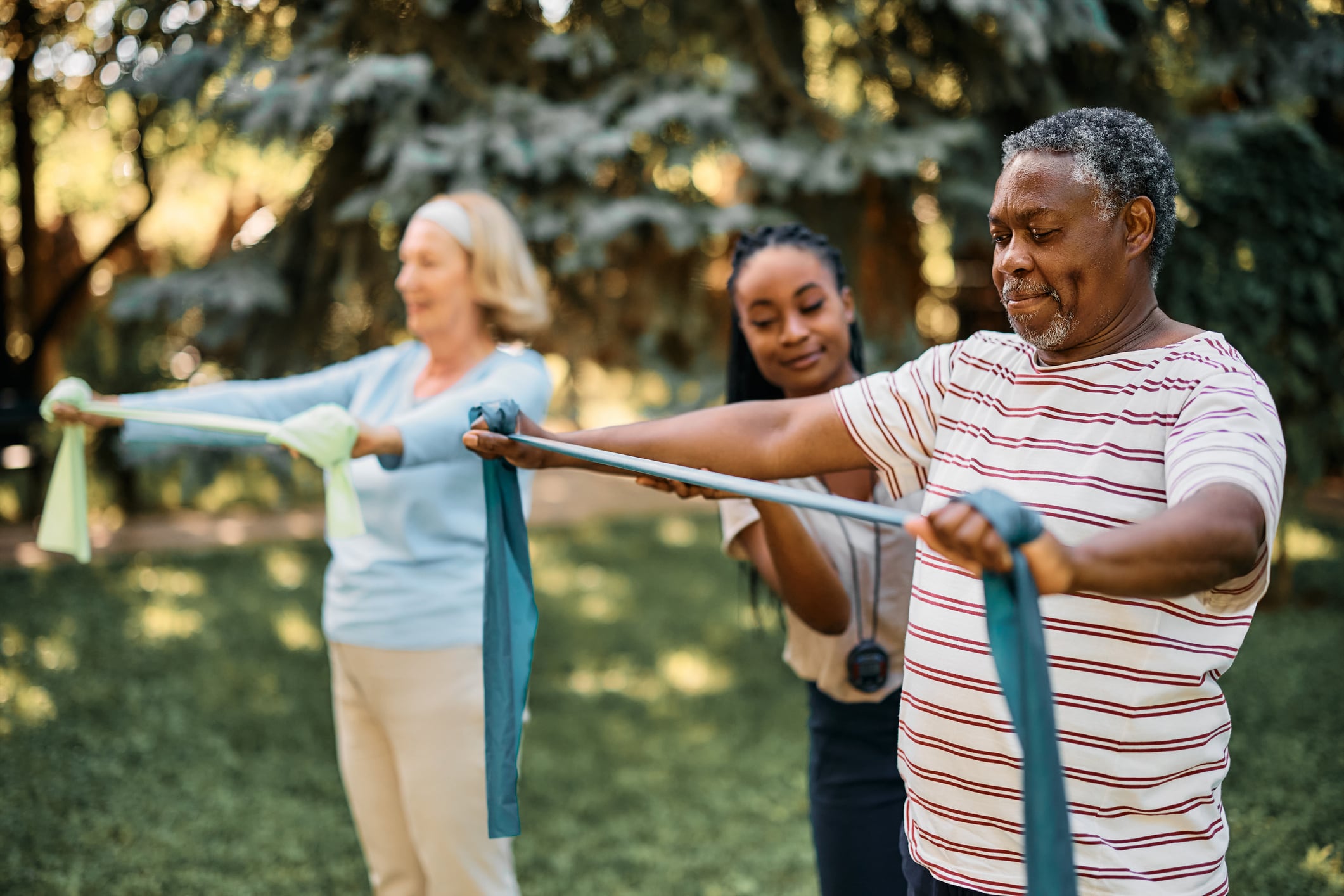 A fitness instructor helping people use exercise bands during an outdoor exercise class.