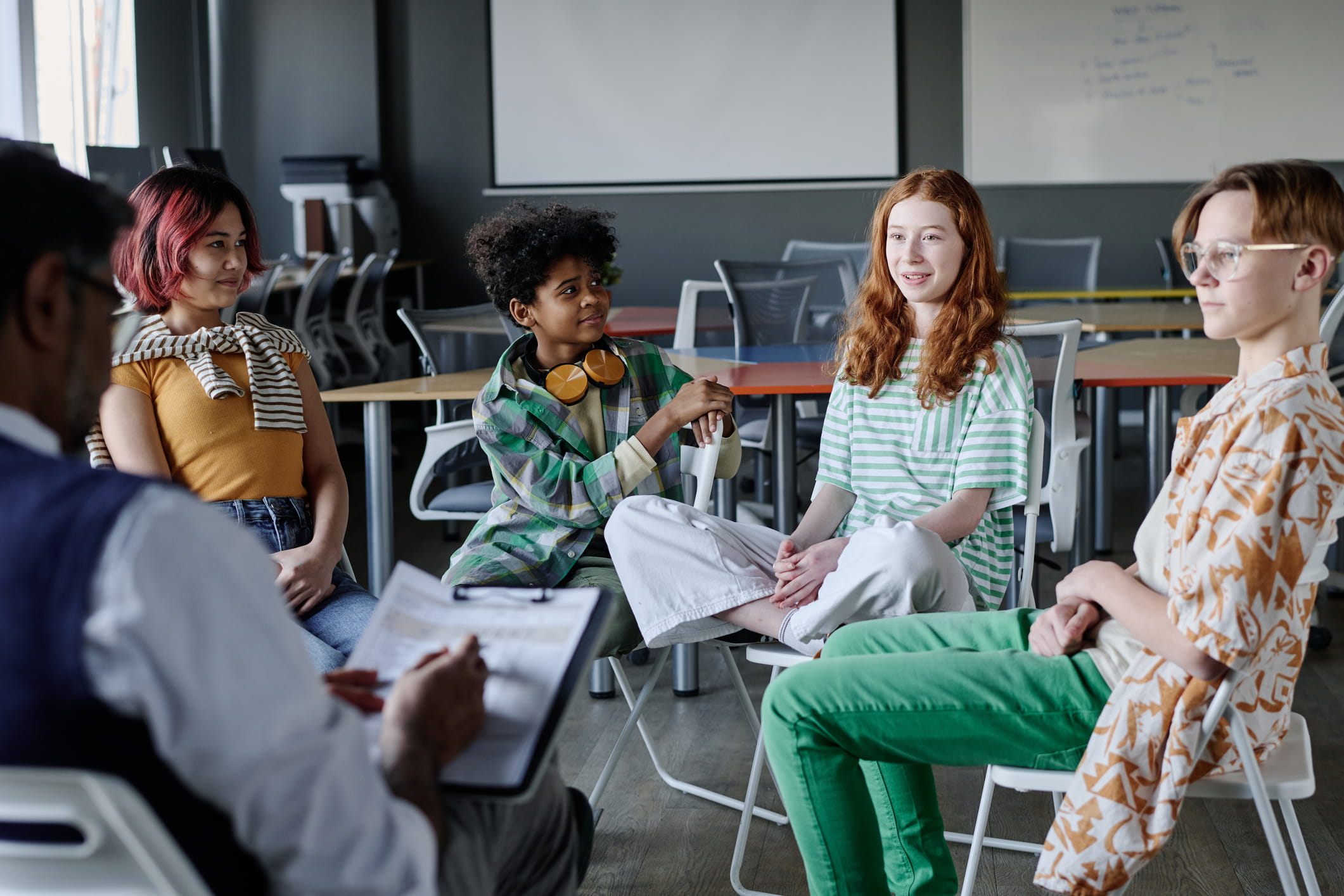 A school counselor takes notes during a group counseling session with students.
