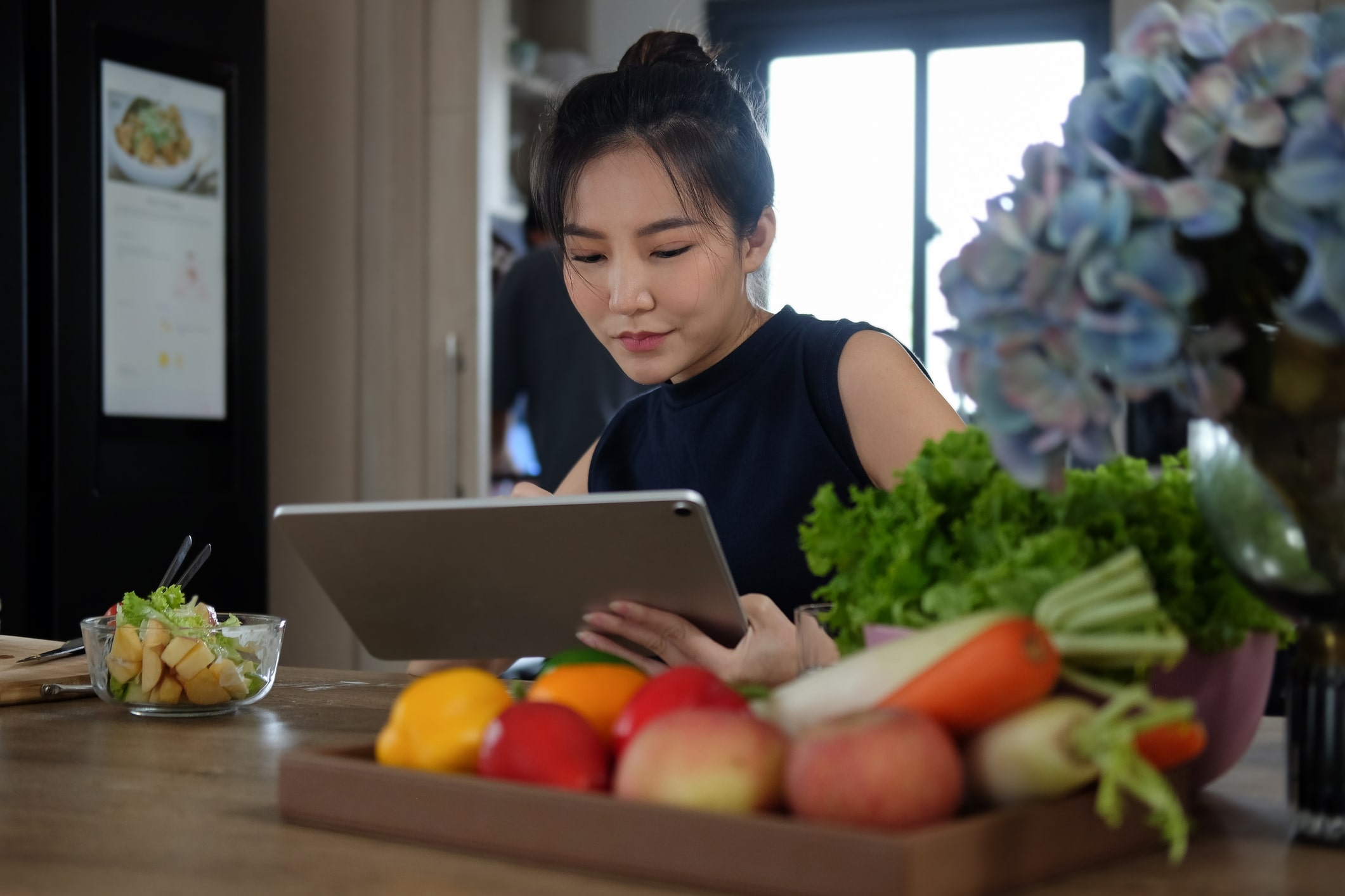 Woman using a tablet while sitting at a table with healthy food on it.