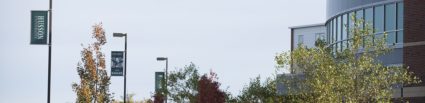 Husson flags on lightpoles, fall foliage and windows on the O'Donnell Commons